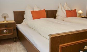 A cozy bedroom with a double bed and orange pillows. Next to the bed is a nightstand with a lamp.