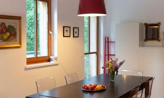 A modern dining area with a long black table and transparent chairs. On the table sits a bowl of colorful fruit and a vase with fresh flowers.