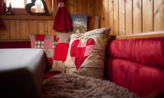 A cozy living area with red cushions and a wood-paneled wall. The cushions have heart-shaped patterns and create a warm atmosphere.