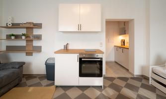 A modern kitchen with a stove and a refrigerator. The room is bright and cheerful, with a cozy sofa and an open design.