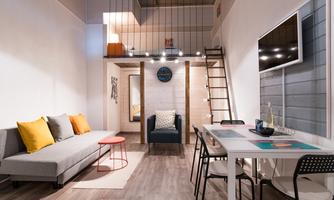 A modern room with a cozy sofa, a table, and a chair. There is a staircase leading to an upper floor, and plenty of natural light.