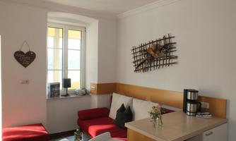 A cozy living room with red sofas and a small table. A window provides plenty of daylight and decorations adorn the walls.