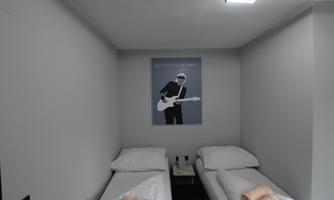 A modern bedroom with two single beds and a minimalist design. A picture of a musician with a guitar hangs on the wall.
