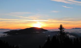 A beautiful sunset over a mountain. The sky is in warm colors and clouds cover the valley.