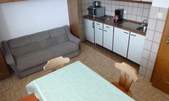 A cozy kitchen with a dining area and a beige sofa. The kitchen is modern and well-equipped.