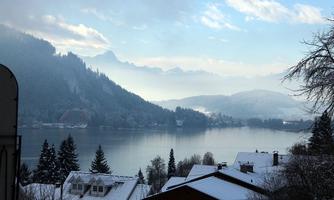 A winter landscape with snow-covered mountains and a tranquil lake. The gentle morning atmosphere is framed by light fog.