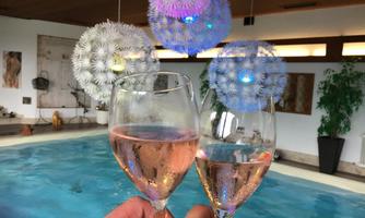 Two glasses of rosé wine toast in front of an indoor pool. In the background, colorful decorative lights and plants can be seen.