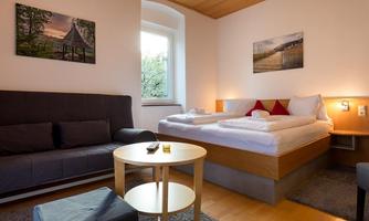 A cozy room with a double bed and a sofa bed. Drinks are on the table and the walls are decorated with pictures.