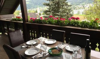 A beautifully set table on a terrace overlooking a picturesque landscape. Flowers adorn the balcony, creating an inviting atmosphere.