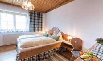 A cozy bedroom with two beds and a wooden wardrobe. On the table, there is a bowl of fresh fruit.