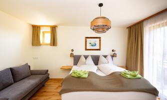 A cozy room with a double bed and a sofa bed. It has bright walls, large windows, and a modern lamp.