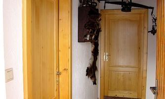 A hallway with two wooden doors and a cobblestone floor. Some decorative items are hanging on the wall.