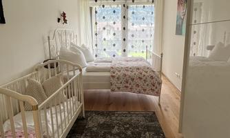 A bright room with a children's bed and a large bed. The windows let in a lot of light and the floor is covered with a carpet.