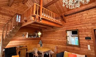 A cozy wooden house with rustic design and warm colors. The room features a staircase, a dining table, and an elegant ceiling light.