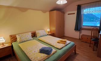 A cozy bedroom with a double bed, lamps, and wooden wardrobes. There are fresh towels on the beds and a window overlooking the outside.