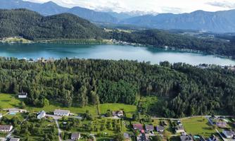A picturesque landscape with a lake, surrounded by mountains and forests. Small houses and green meadows lie around it.
