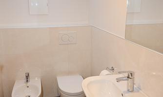 A modern bathroom with a sink, a bidet, and a toilet. The walls are bright and designed with large tiles.