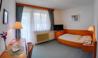 A simple hotel room with a bed, a desk, and a television. Large windows provide plenty of natural light.