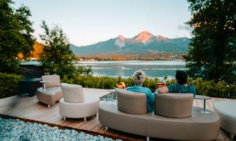 A relaxed terrace with modern seating that offers a beautiful view of the lake and the surrounding mountains. The atmosphere is peaceful and inviting.