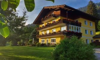 A charming yellow house with several balconies and flower boxes. Surrounded by green grass and trees, it radiates an inviting atmosphere.
