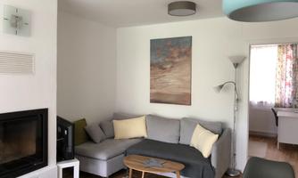 A cozy living room with a gray couch and cushions. A picture hangs on the wall, and an elegant table is in the room.