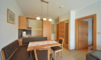 A modern kitchen with a wooden dining area. Bright light falls through the windows into the room.