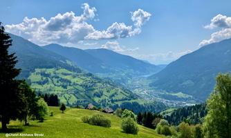 A picturesque valley with gentle hills and high mountains in the background. The sky is clear and interspersed with some clouds.
