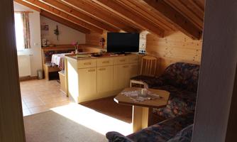 A cozy attic apartment with wooden ceilings and a living area. The room features a sofa, a table, and a TV.
