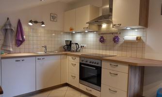 A modern kitchen with white cabinets and a stainless steel sink. The lighting is friendly and there are appliances like a stove and a coffee machine.