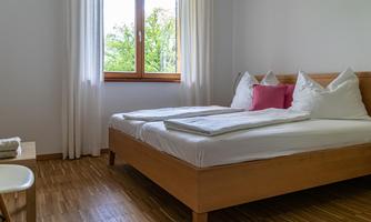 A bright bedroom with a double bed and large windows. There are white curtains and a pleasant atmosphere.