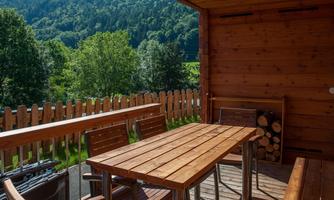 A cozy balcony with a wooden table and chairs. In the background, green trees and a picturesque landscape are visible.
