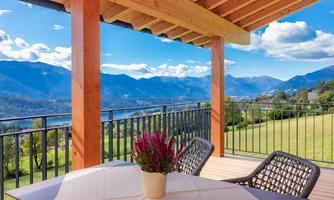 A beautiful terrace with a table and chairs, surrounded by an impressive mountain landscape. In the foreground, there is a pot of flowers.