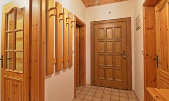 An inviting hallway with wooden paneling and a large front door. The walls are in light tones, and there is a simple tile pattern on the floor.