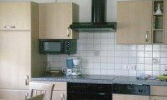 A modern kitchen with light wooden furniture. It features a refrigerator, a microwave, and a stove.