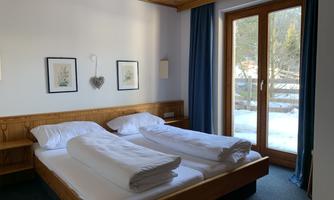 A cozy room with two beds, white duvets, and wooden interiors. Large windows provide a view of the snow-covered landscape.