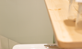 A modern bathroom with a sink and a wooden countertop. The glass door to the shower is visible, and there are shiny fixtures.
