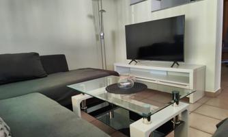 A modern living room with a comfortable sofa and a glass table. The television is on a white TV stand.