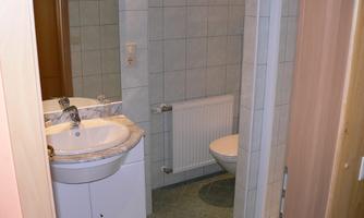 A simple bathroom with two sinks and a shower. The walls are tiled with light tiles.