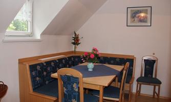 A cozy dining area with a wooden bench and a table. On the table, there is a flower vase with fresh flowers.