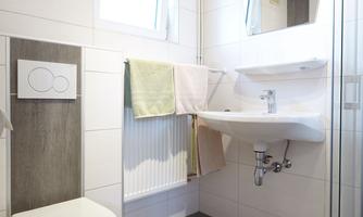 A modern bathroom with a shower, a sink, and a toilet. Bright and welcoming design with large tiles and a wooden ceiling.