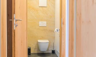 A modern bathroom with a white toilet and a minimalist designed environment. The floor is made of wood and the walls are in soft color tones.