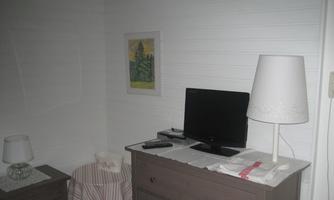 A simple room with a dresser and a television. A lamp and a table with a decorative cloth complement the ambiance.