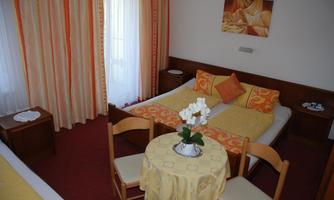 A cozy room with two beds, a round table, and chairs. The color scheme is warm with orange curtains and a small flower pot on the table.
