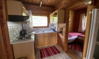 A cozy kitchen with wooden walls and modern amenities. Next door is a bedroom with two single beds.