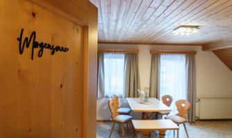 A cozy room with wooden decor and a dining table. The windows are adorned with curtains and let in plenty of daylight.