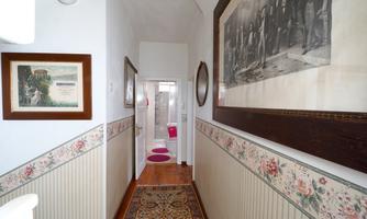 A narrow hallway with decorative pictures on the walls. At the end of the hallway, a bathroom is visible, accessible through a door.
