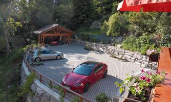 A paved parking lot with two cars and a wooden shelter. Surrounded by trees and plants, the place offers a peaceful atmosphere.