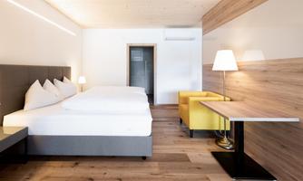 A modern hotel room with two beds and hardwood floors. There is a yellow seating area and warm light from the lamps.