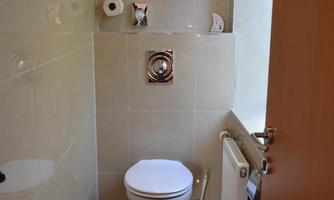 A small bathroom with a toilet and bright tiles. On the wall, there are toilet paper holders and a radiator.