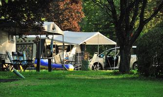 A beautiful campsite with tents and a green lawn. In the background, there is a car and garden furniture.